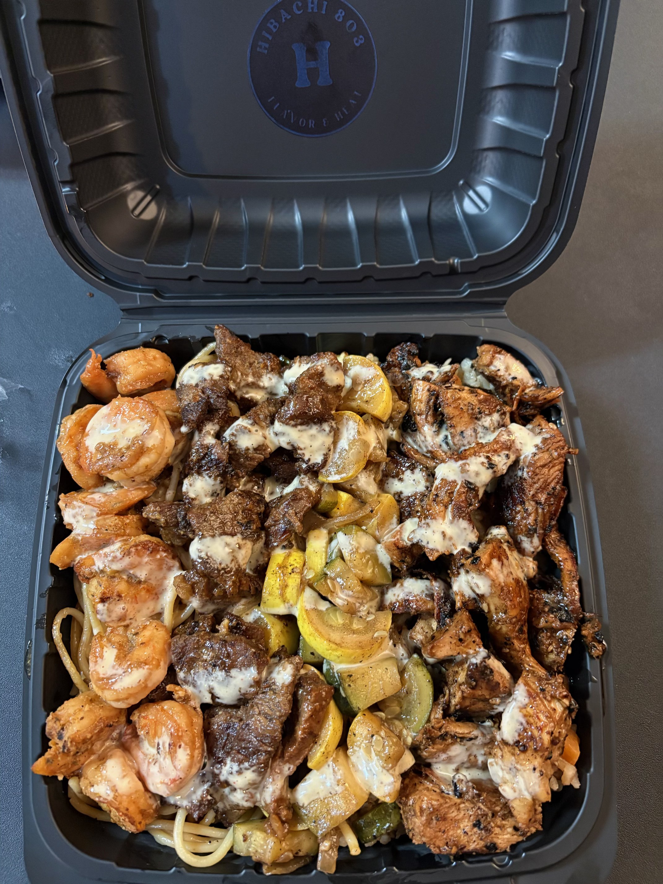Hibachi 803 takeout box with steak, chicken, shrimp, noodles, and yum yum sauce